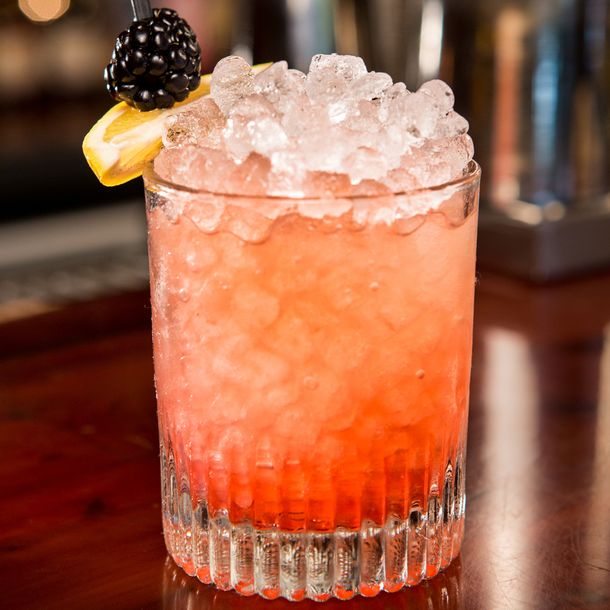 A beautiful Bramble cocktail served in a tumbler with shaved ice and blackberry garnish