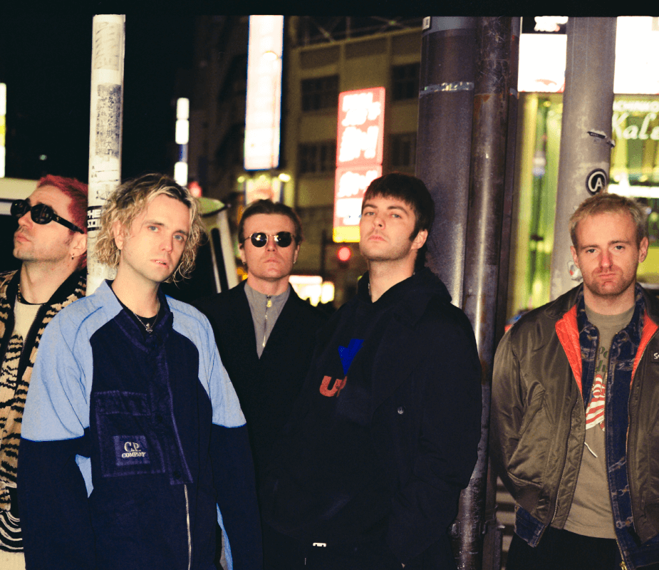 Fontaines DC stand on the road in various outfits, at nighttime 