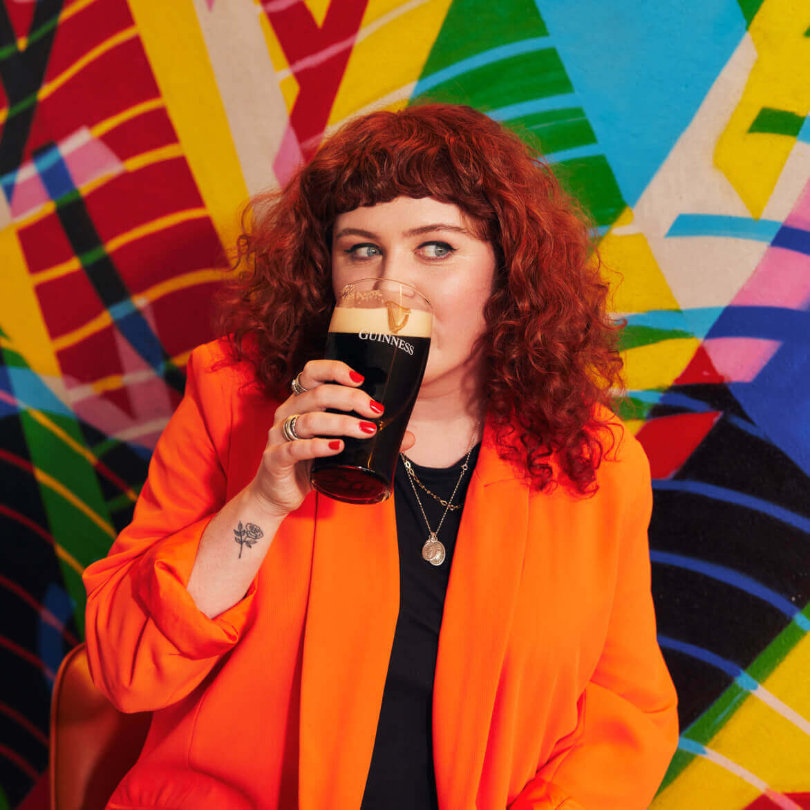 Woman wearing a orange suit drinking a pint of Guinness 