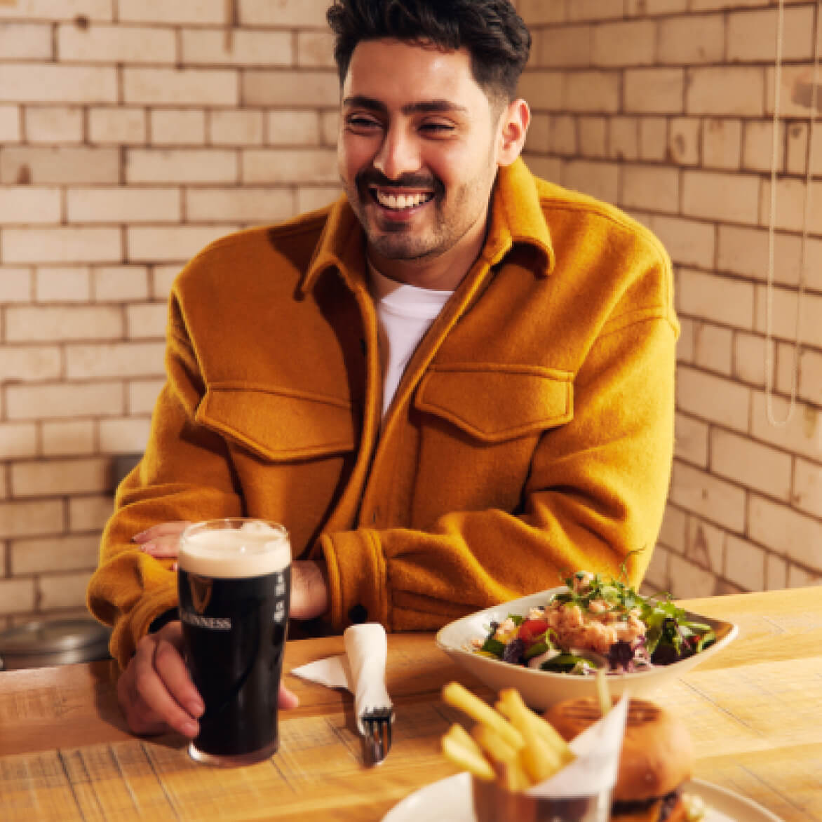 A cheerful man holding a pint of Guinness paired with our Atlantic house smoked salmon on a salad of gold river farms leaves.