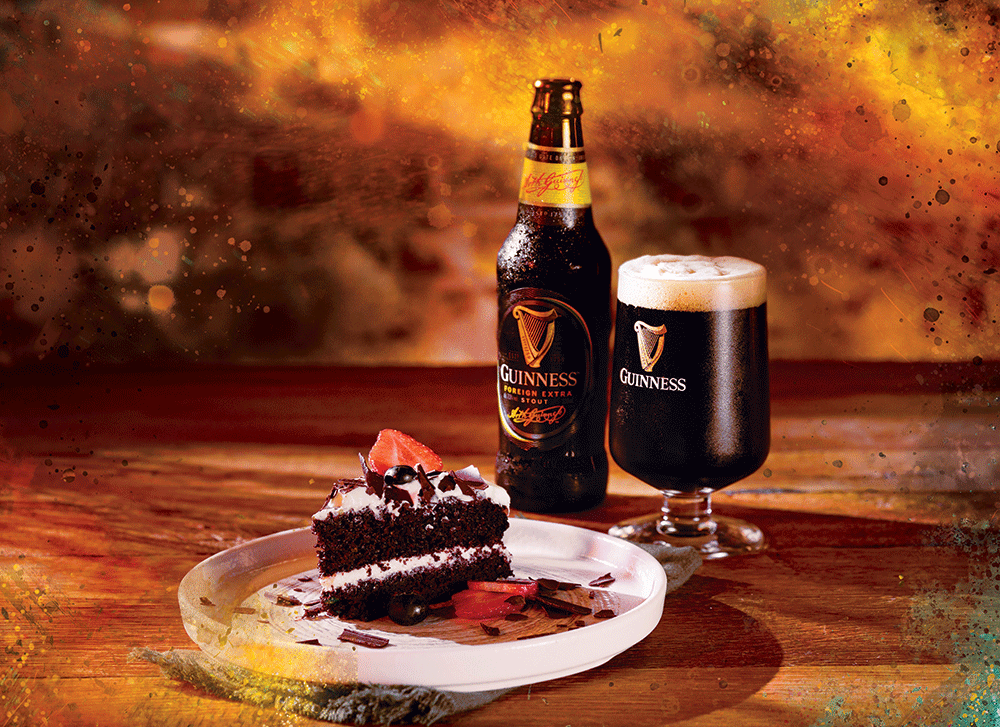 Slice of Guinness chocolate cake on a plate beside a glass of Guinness and bottle of Guinness Foreign Extra Stout