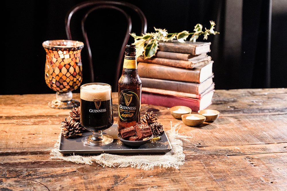 Guinness truffles on a wooden table beside a glass of Foreign Extra Stout