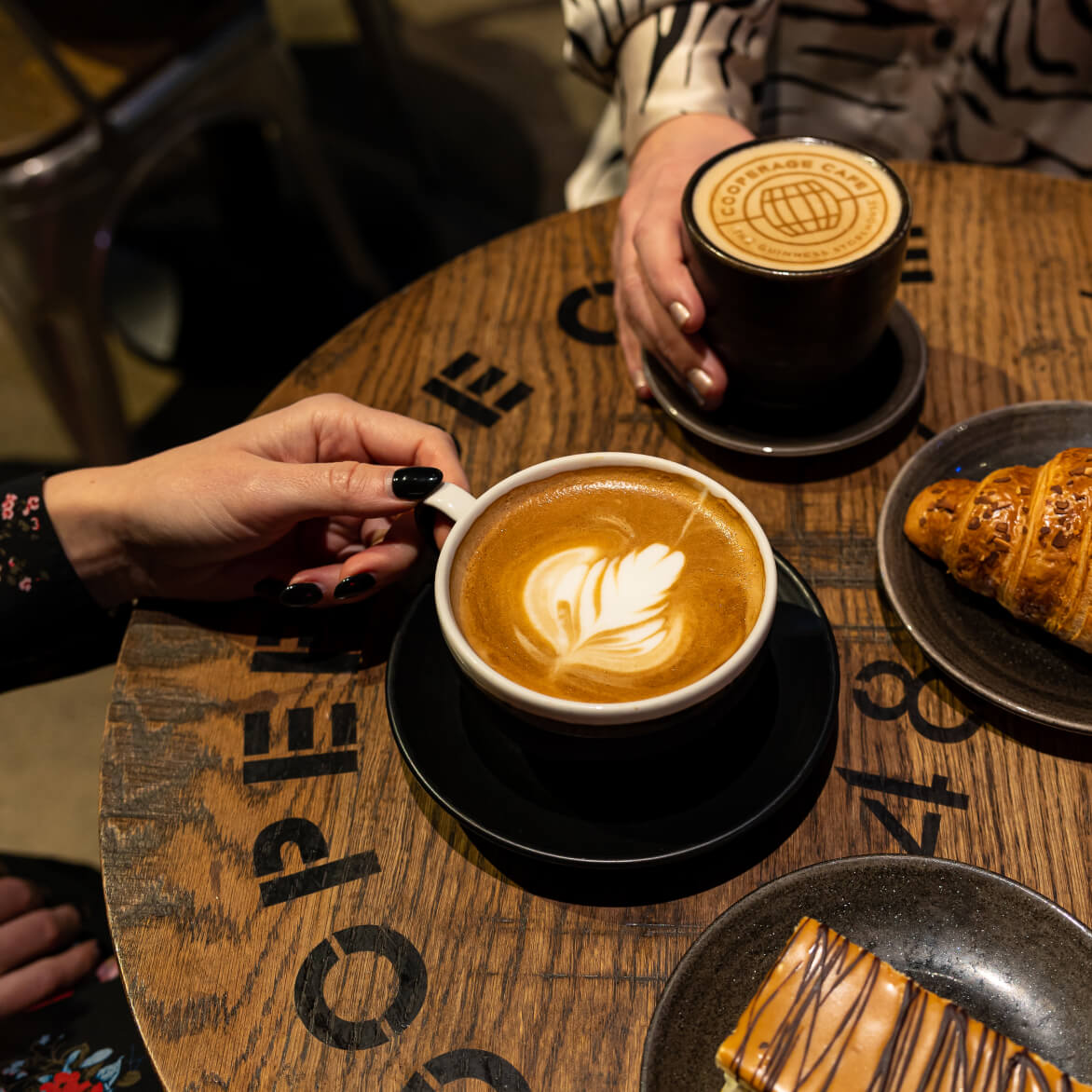 A relaxing time in the Cooperage Café where two people are enjoying their stylised drinks and freshly-baked treats while on their tour. 