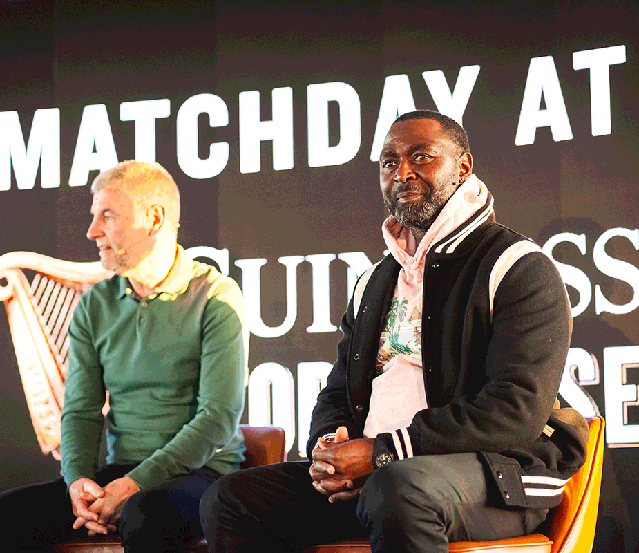 Andy Cole and Dennis Irwin sitting in front of a black wall with white writing on stage at the Guinness Storehouse