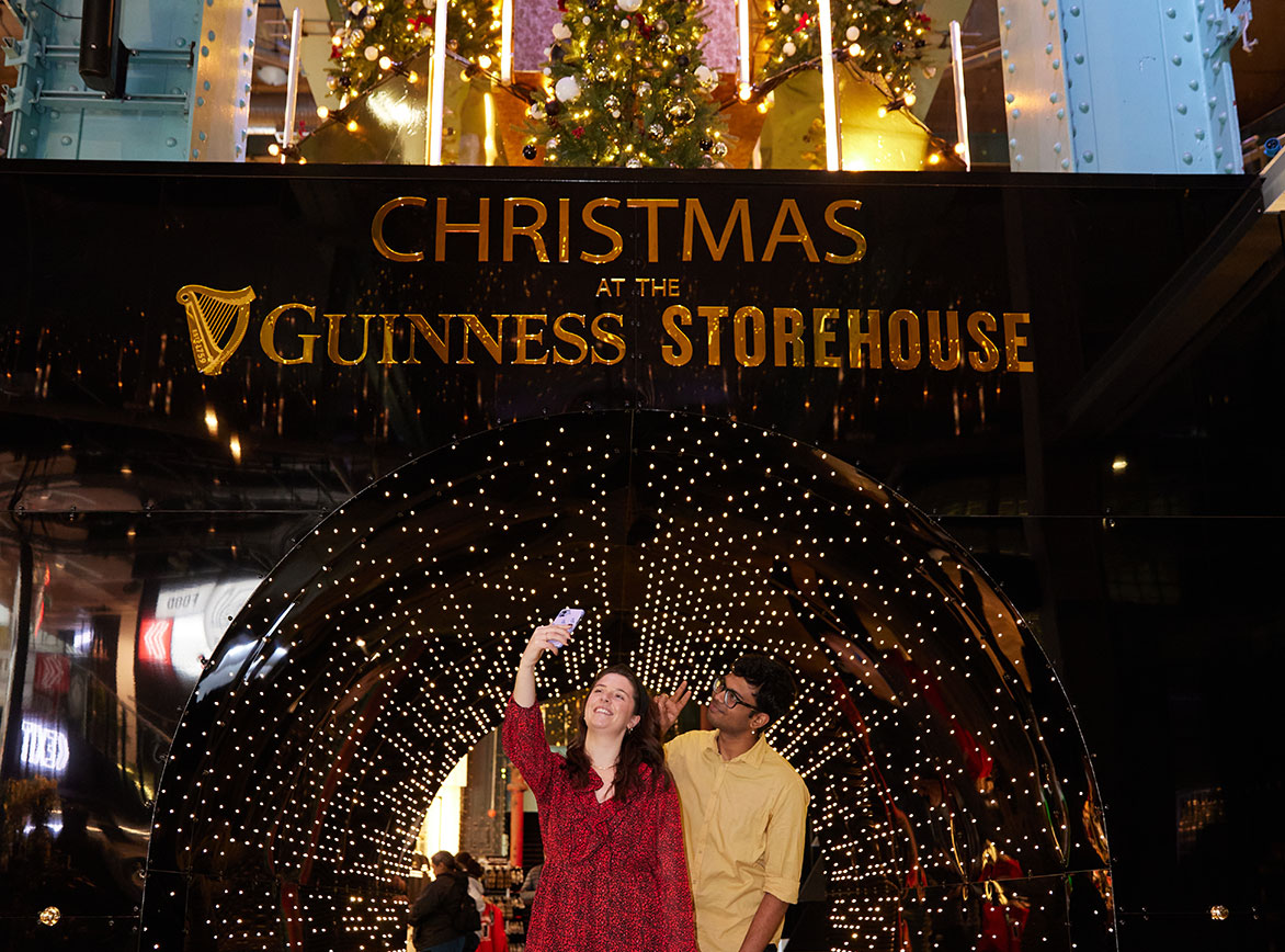A man and woman take a selfie in front a large Christmas tree in Guinness Storehouse 