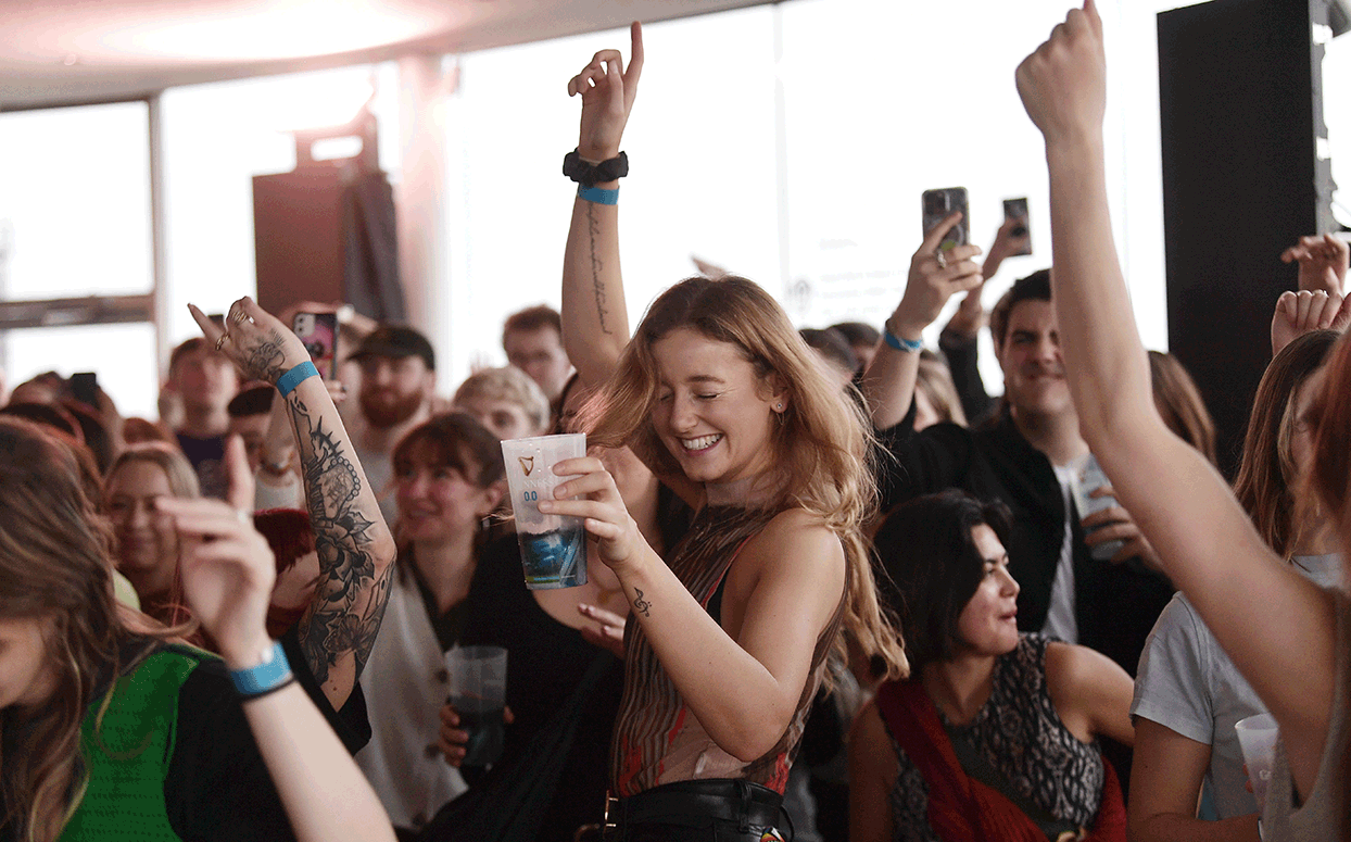 A young woman dances in the middle of a crowd at the Gravity bar in the Guinness Storehouse, with her arm in the arm, surrounded by people
