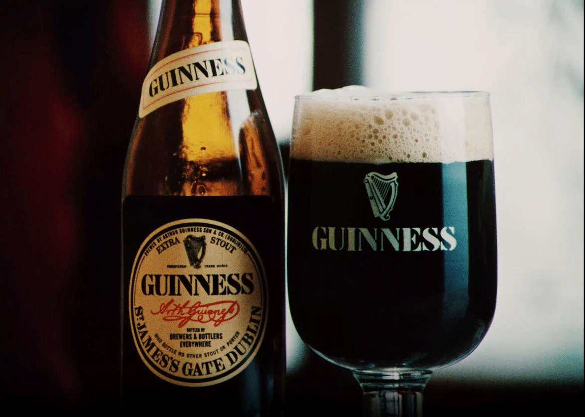 An old style glass of Guinness next to a bottle of it