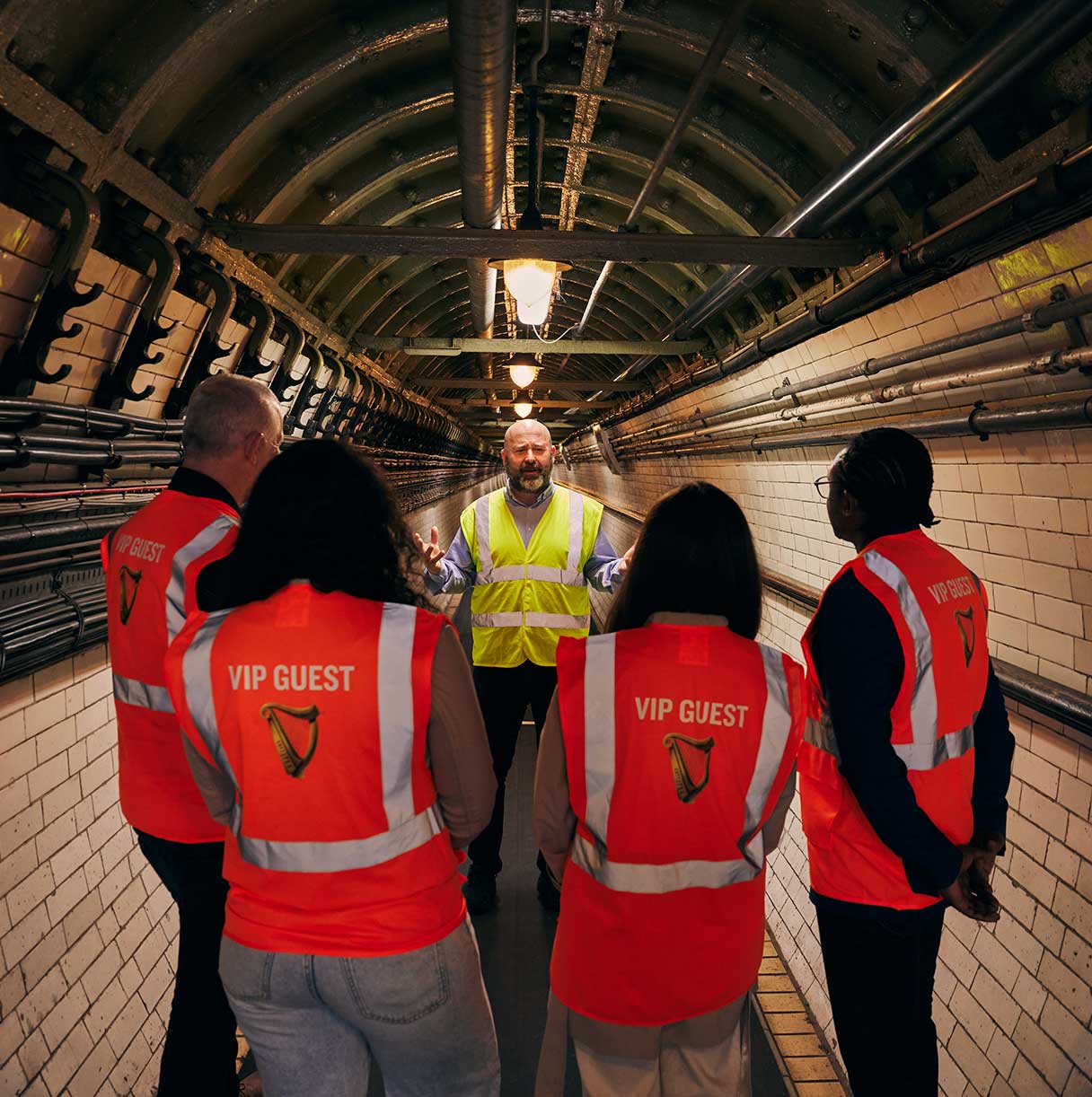 A Guinness tour guide stands in an underground tunnel with four VIP guests, all wearing high vis