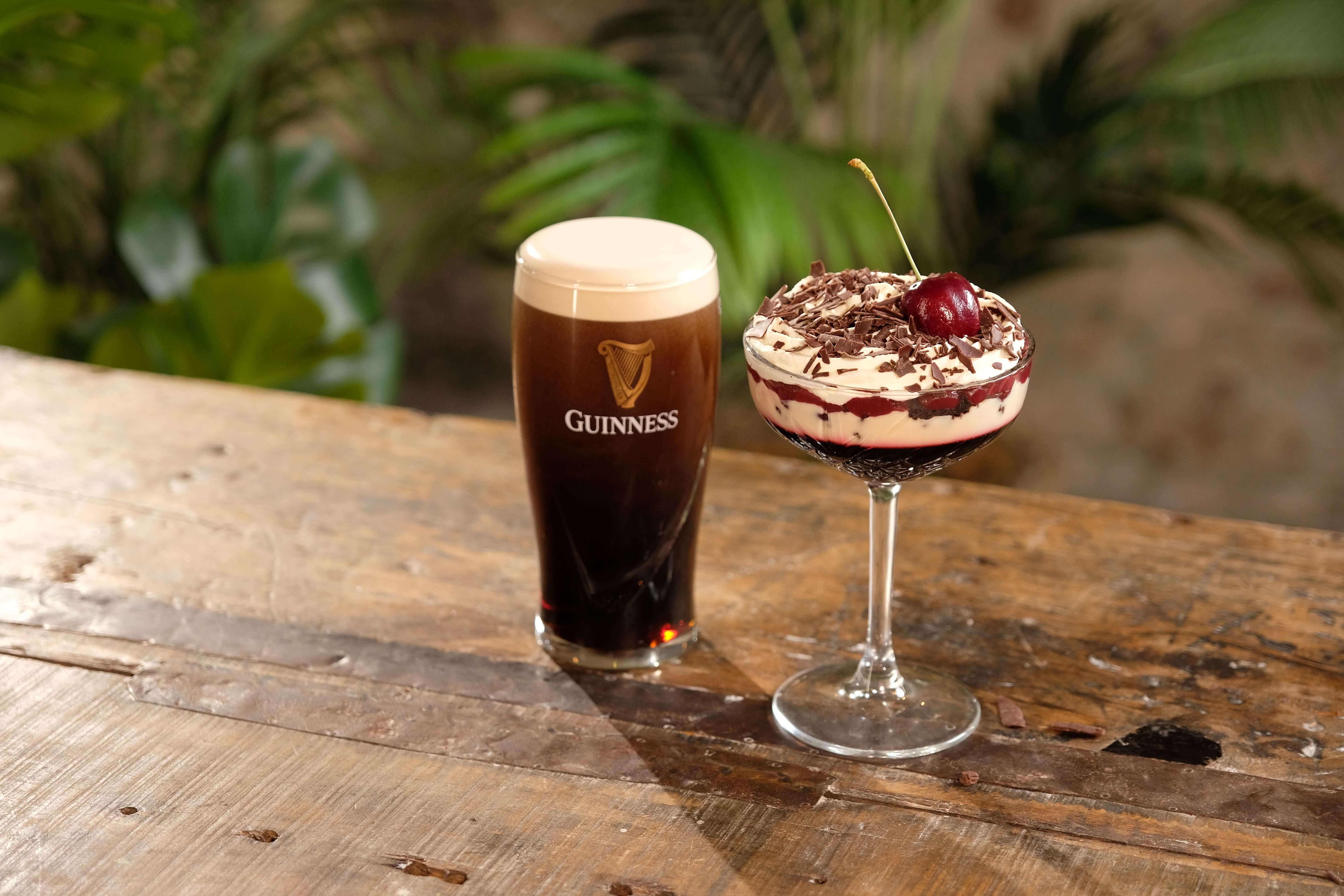 A Guinness and cherry trifle on a table beside a pint of Guinness.