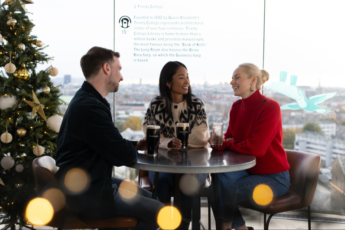 Three friends - 2 women and a man enjoying pints of guinness and a glass of water at the the Gravity Bar decorated with Christmas trees and baubles