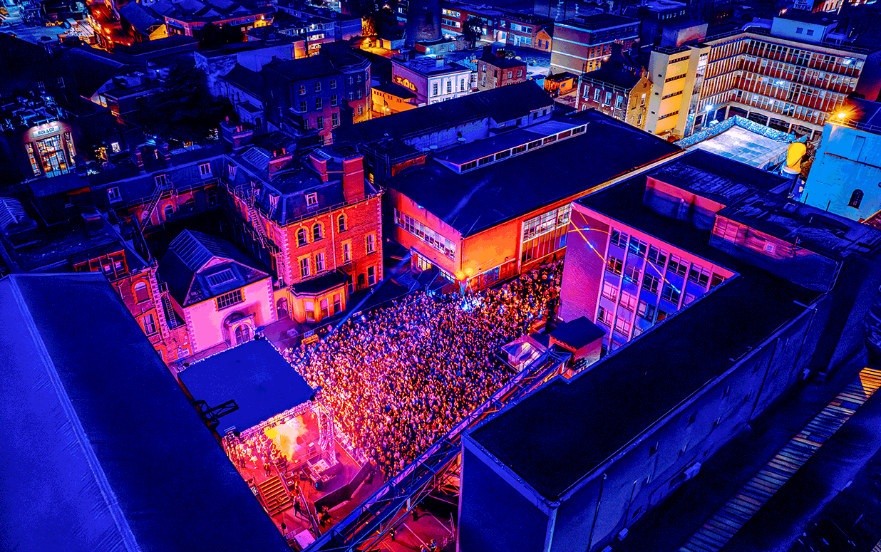 Aerial view of a concert on the St James Gate site of Guinness, people in a crowd surrounded by buildings