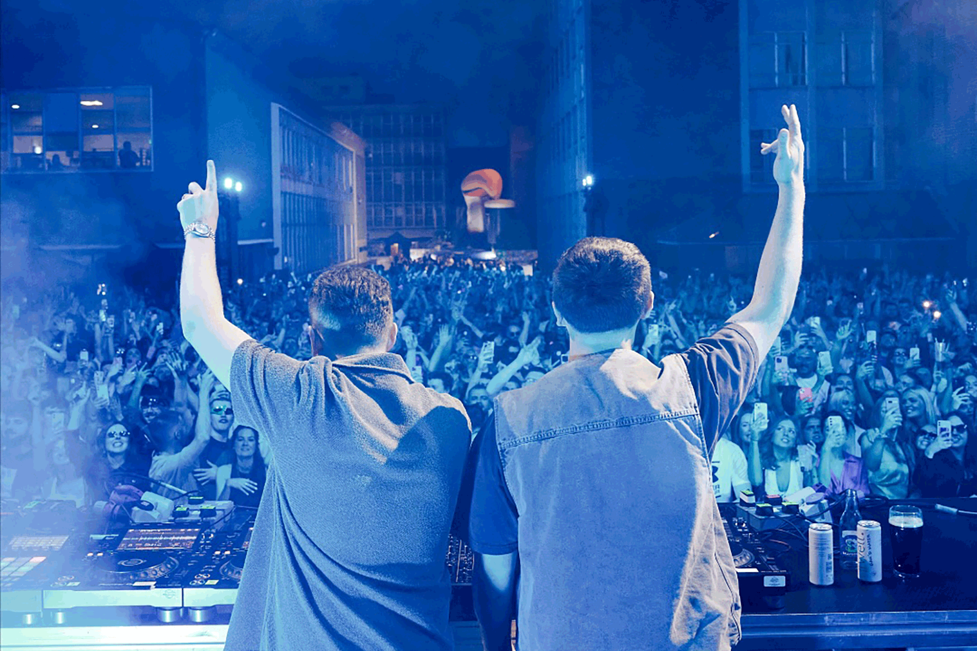 DJ duo Disclosure are photographed from behind, arms in the arm, standing on a stage in front of a large crowd