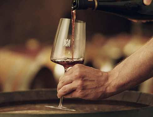 A bottle of Pinot Noir German wine poured into a wine glass on top of a barrel